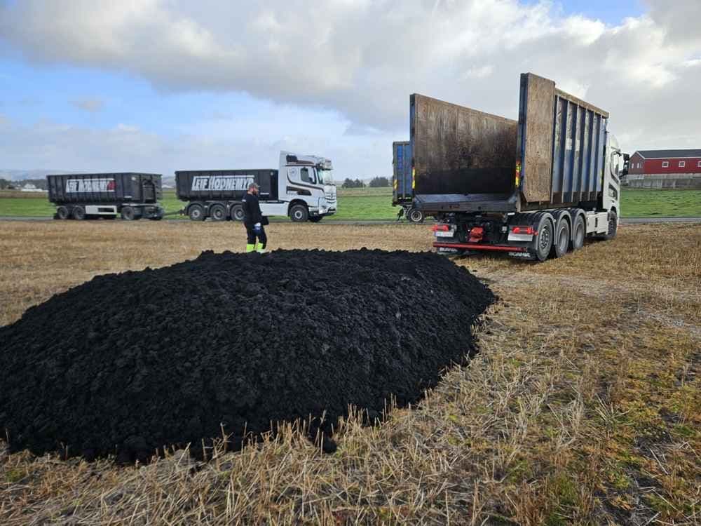 Levering av biorest på et jorde med stor lastebil med container. Foto.