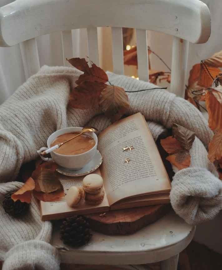 Stol med bok og kaffe på, med høstløv rundt. Stemningsbilde.
