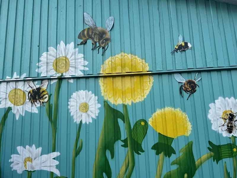 Husvegg med påmalte blomster, humler og bier. Foto. 