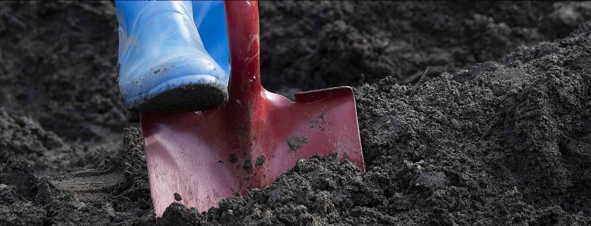 Støvler som trykker ned en spade i jord. Foto. 