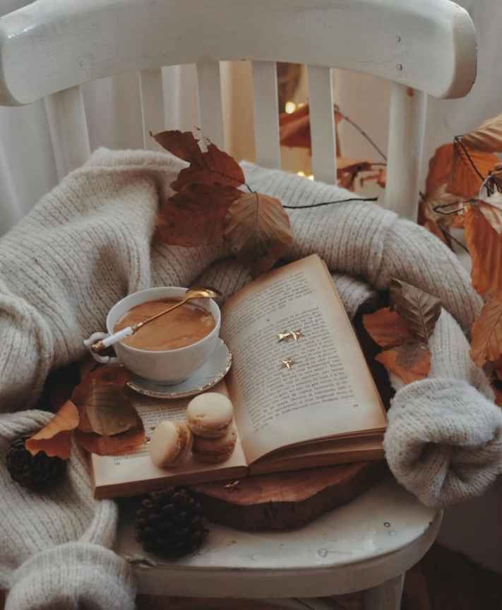 Stol med bok og kaffe på, med høstløv rundt. Stemningsbilde.